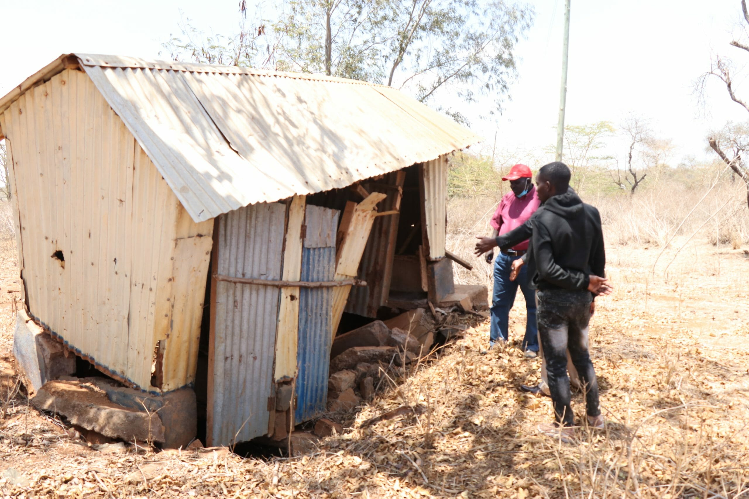 The old toilet block with iron sheet walls and doors with 2 men in front