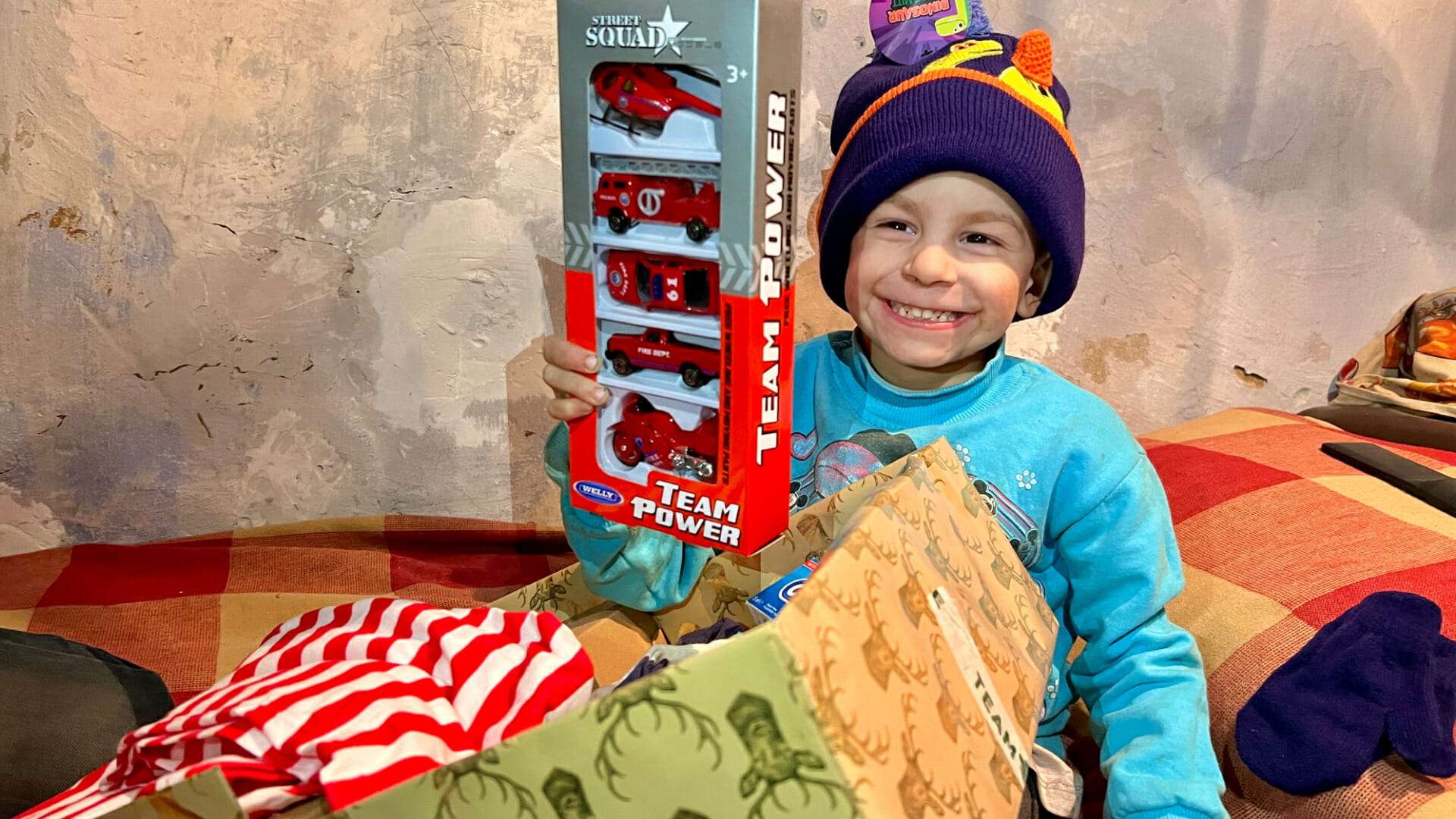 Boy smiling holding a pack of 5 toys cars.